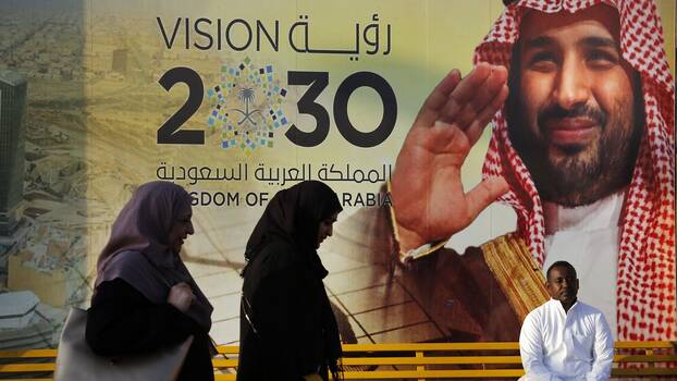 People walk past a banner showing Saudi Crown Prince Mohammed bin Salman, outside a mall in Jiddah, Saudi Arabia, Friday, Dec. 6, 2019