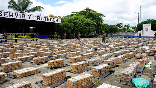 Ecuadorian police officers guard stacked packages of cocaine being presented to journalists.