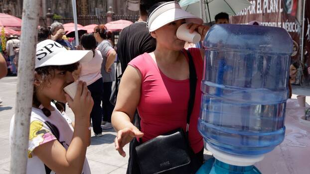 Hohe Temperaturen in Mexiko-Stadt. Eine Frau trinkt Wasser aus einem Wasserspender, um sich zu erfrischen, während sie auf dem Hauptplatz von Mexiko-Stadt spazieren geht. am 26. Mai 2024 