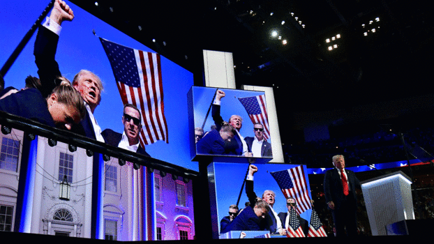 Donald Trump steht neben mehreren Großbildschirmen, die ihn unmittelbar nach dem Attentat in heroischer Pose zeigen.